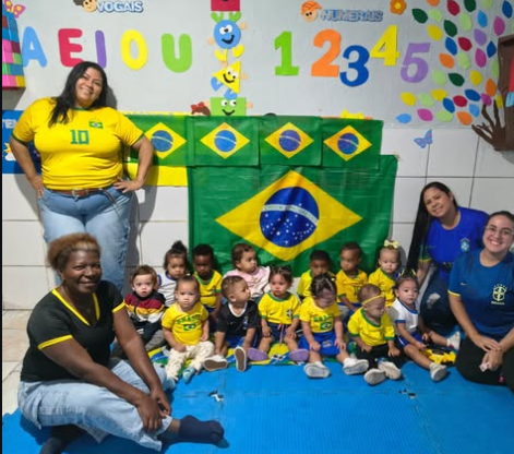 Bebês da creche em sala decorada com alfabeto, acompanhados pelas educadoras